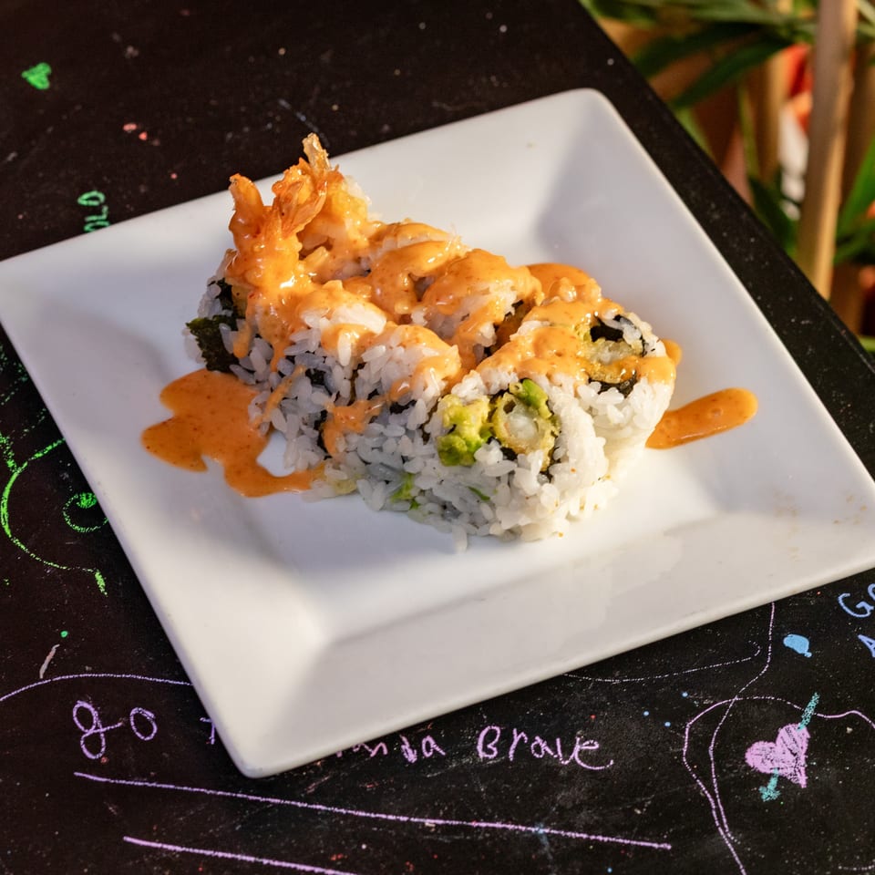 Sushi rolls with tempura shrimp and avocado, drizzled with orange sauce, on a white plate.