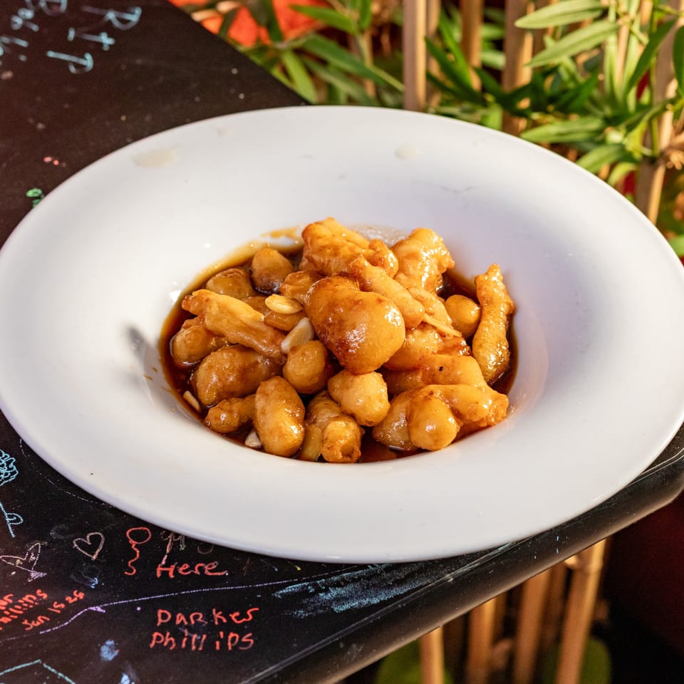 A white bowl filled with golden-brown chicken pieces in a rich, dark sauce, on a dark table.